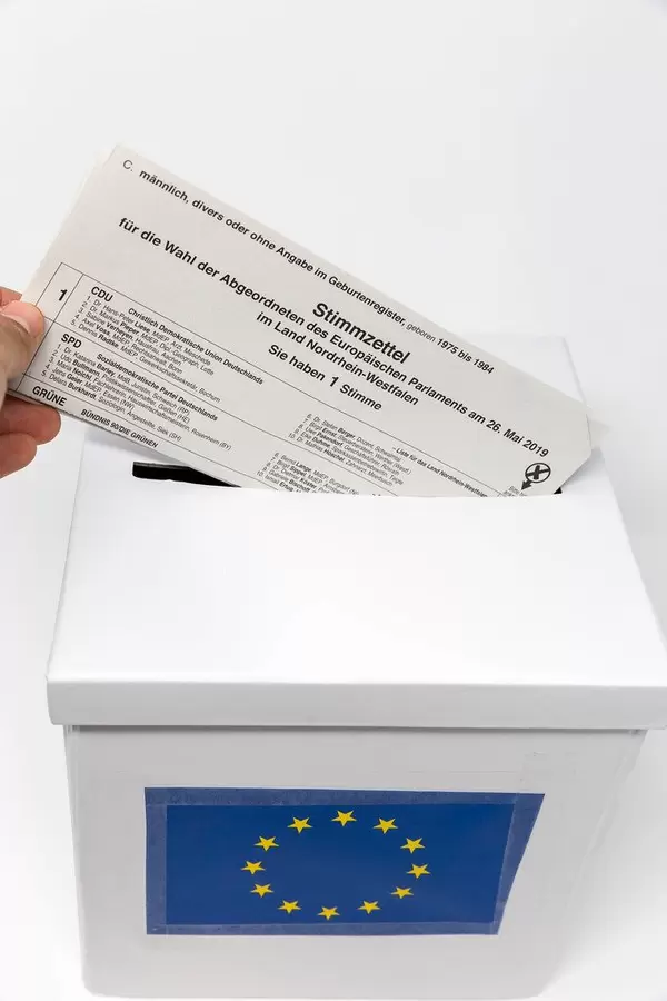Hand steckt den Europawahl-Stimmzettel für Briefwähler symbolisch in eine Abstimmungsurne