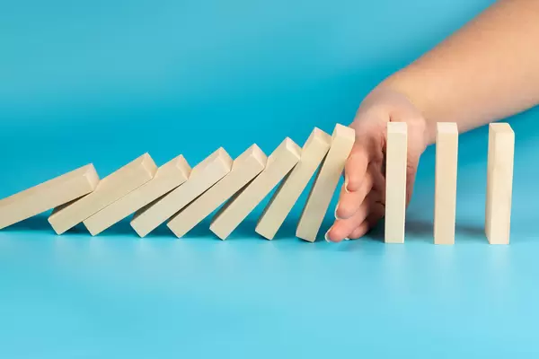 Hand stopping wooden blocks from falling in the line of domino, blue background