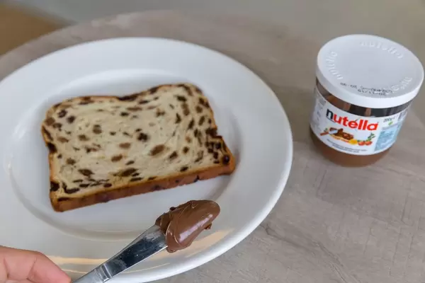 Hand streicht Nutella mit Messer auf Brot mit Früchten und Rosinen