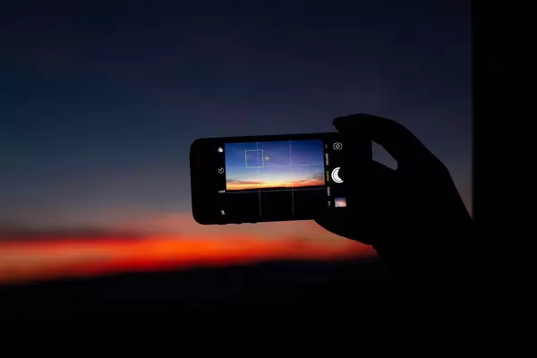 Hand taking photo of a pink sunset with a phone