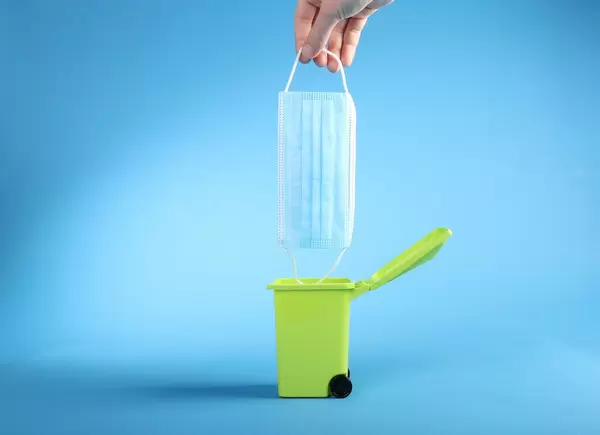 Hand throwing medical face mask into trash can