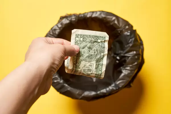 Hand throwing money into trash bin