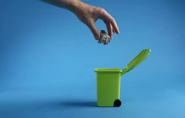 Hand throwing money into trash can
