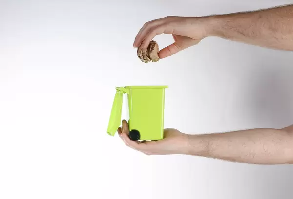 Hand throwing out paper into a trash container