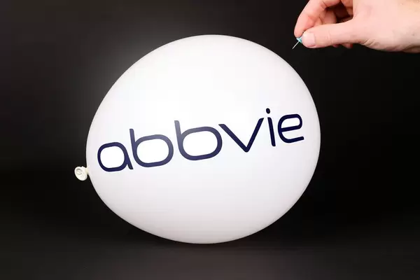 Hand uses a needle to burst a balloon with AbbVie logo