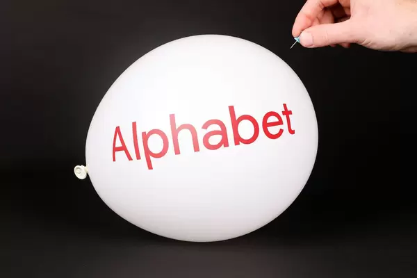 Hand uses a needle to burst a balloon with Alphabet Inc logo