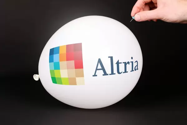 Hand uses a needle to burst a balloon with Altria logo