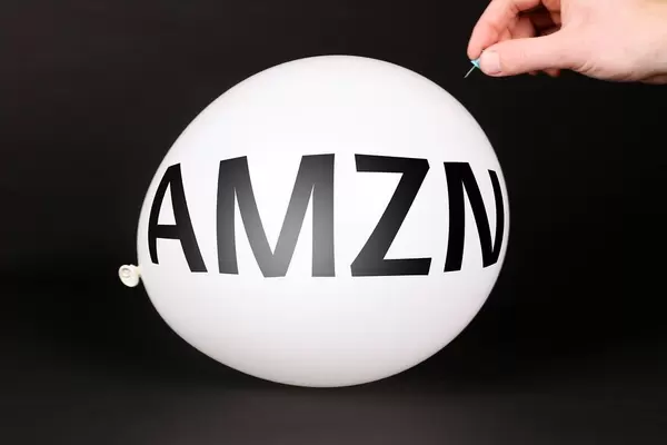 Hand uses a needle to burst a balloon with AMZN text