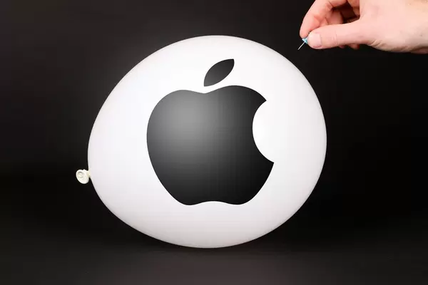 Hand uses a needle to burst a balloon with Apple logo