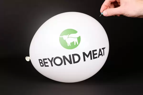 Hand uses a needle to burst a balloon with Beyond Meat logo
