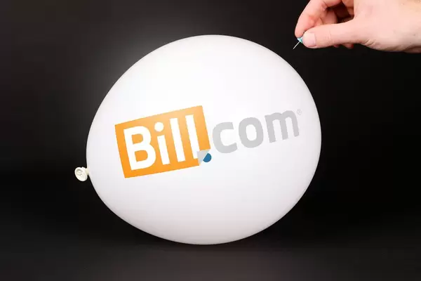Hand uses a needle to burst a balloon with Bill.com logo