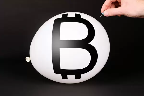 Hand uses a needle to burst a balloon with Bitcoin symbol
