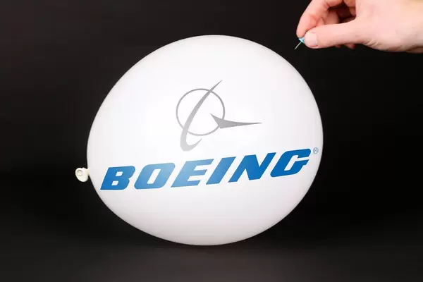 Hand uses a needle to burst a balloon with Boeing logo