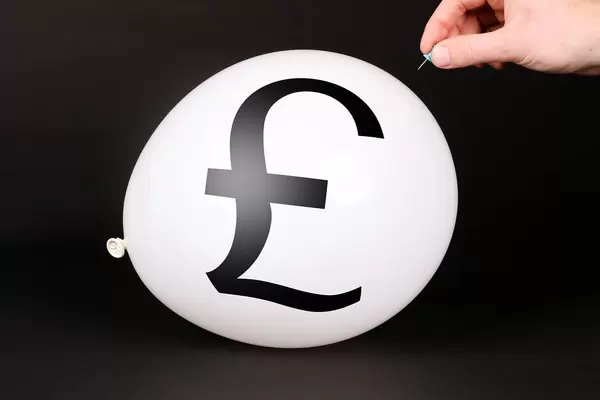 Hand uses a needle to burst a balloon with British Pound