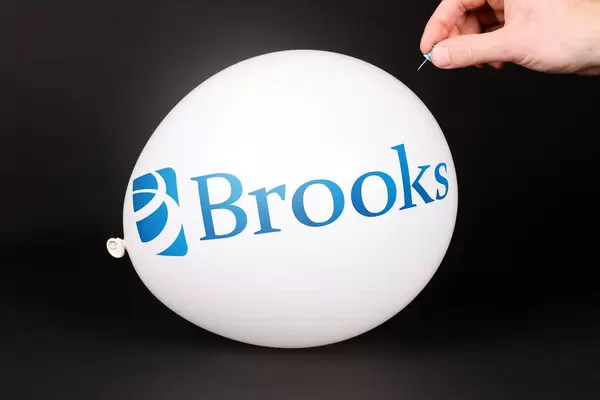 Hand uses a needle to burst a balloon with Brooks logo
