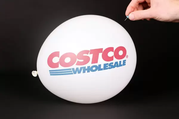 Hand uses a needle to burst a balloon with Costco logo
