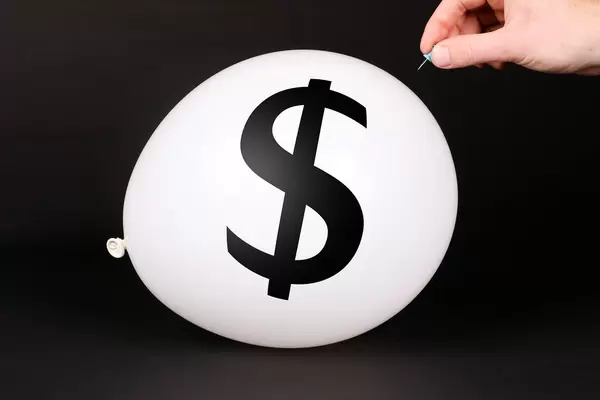 Hand uses a needle to burst a balloon with Dollar symbol