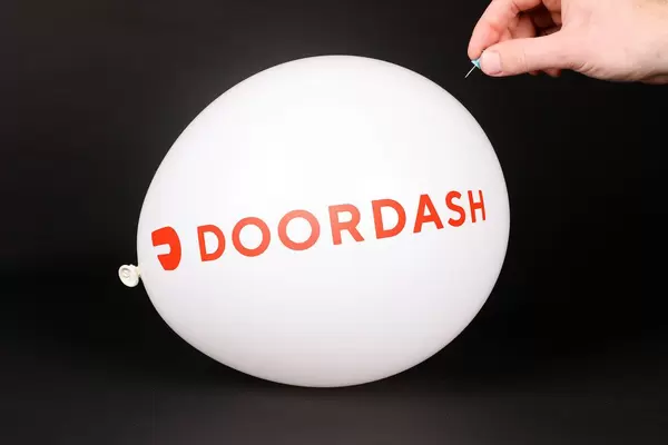 Hand uses a needle to burst a balloon with DoorDash logo