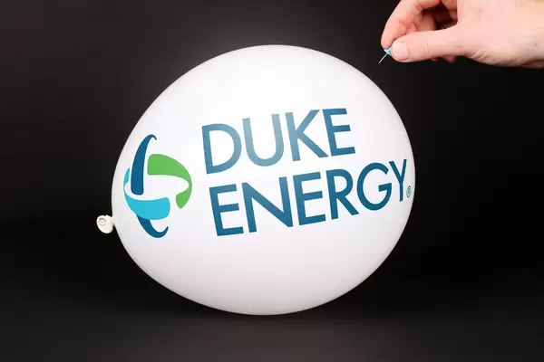 Hand uses a needle to burst a balloon with Duke Energy logo