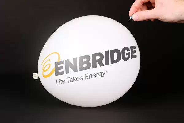 Hand uses a needle to burst a balloon with Enbridge logo