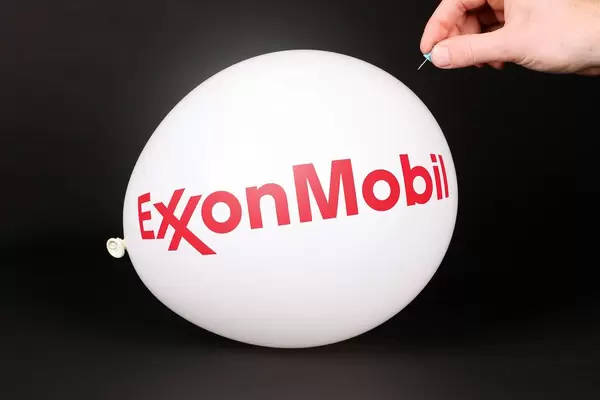 Hand uses a needle to burst a balloon with ExxonMobil logo