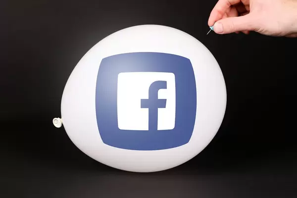 Hand uses a needle to burst a balloon with Facebook icon