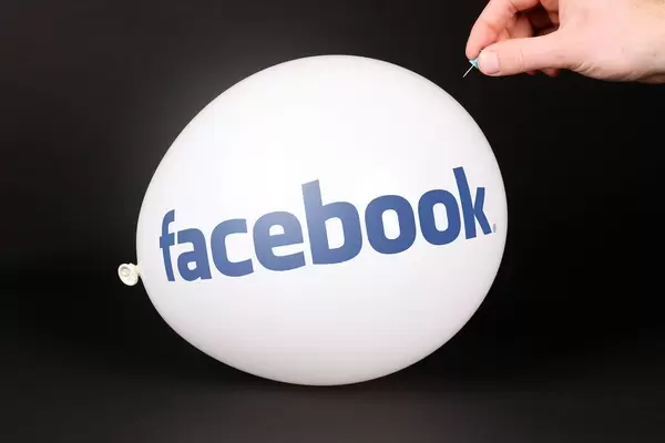Hand uses a needle to burst a balloon with Facebook logo