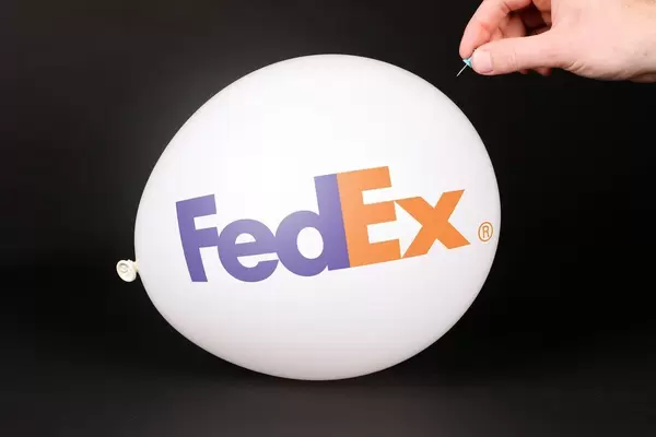 Hand uses a needle to burst a balloon with FedEx logo