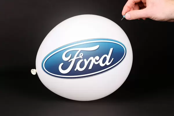 Hand uses a needle to burst a balloon with Ford logo
