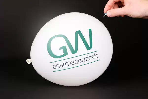 Hand uses a needle to burst a balloon with GW Pharmaceuticals logo