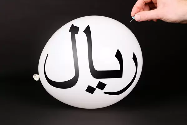 Hand uses a needle to burst a balloon with Iranian Rial symbol