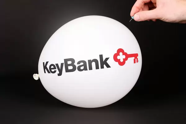 Hand uses a needle to burst a balloon with KeyBank logo