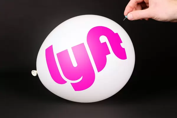 Hand uses a needle to burst a balloon with Lyft logo