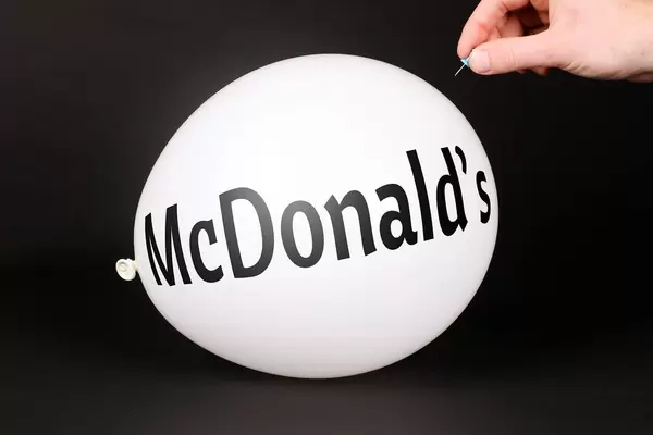 Hand uses a needle to burst a balloon with McDonald's text