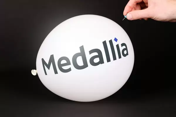 Hand uses a needle to burst a balloon with Medallia logo