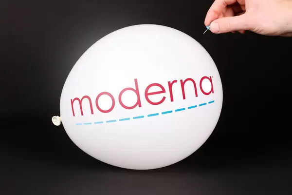 Hand uses a needle to burst a balloon with Moderna logo