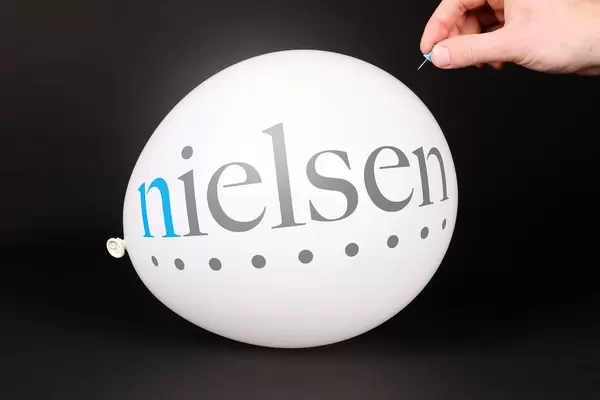 Hand uses a needle to burst a balloon with Nielsen logo