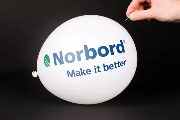 Hand uses a needle to burst a balloon with Norbord logo