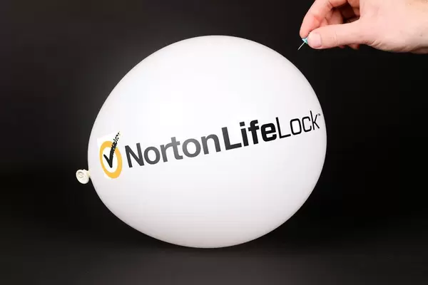 Hand uses a needle to burst a balloon with Norton LifeLock logo