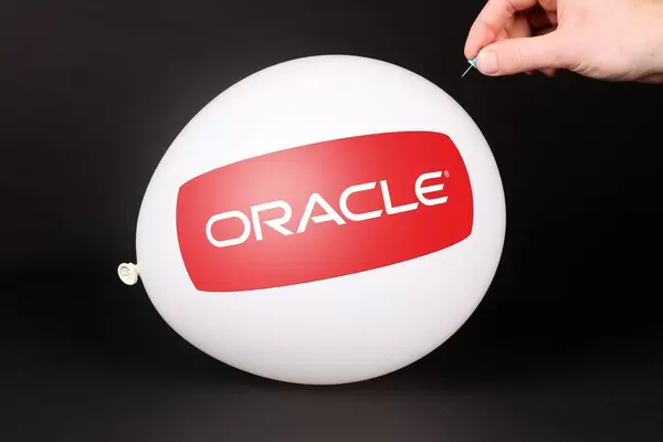 Hand uses a needle to burst a balloon with Oracle logo