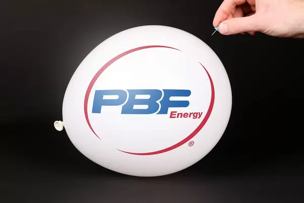 Hand uses a needle to burst a balloon with PBF Energy logo