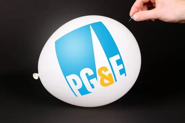 Hand uses a needle to burst a balloon with PG&E logo