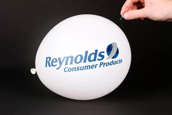 Hand uses a needle to burst a balloon with Reynolds Consumer Products logo