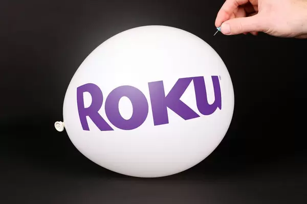 Hand uses a needle to burst a balloon with Roku logo