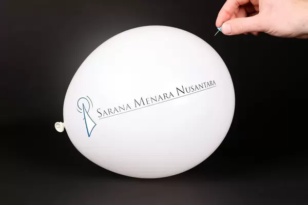 Hand uses a needle to burst a balloon with Sarana Menara Nusantara logo