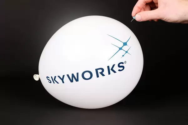 Hand uses a needle to burst a balloon with Skyworks logo