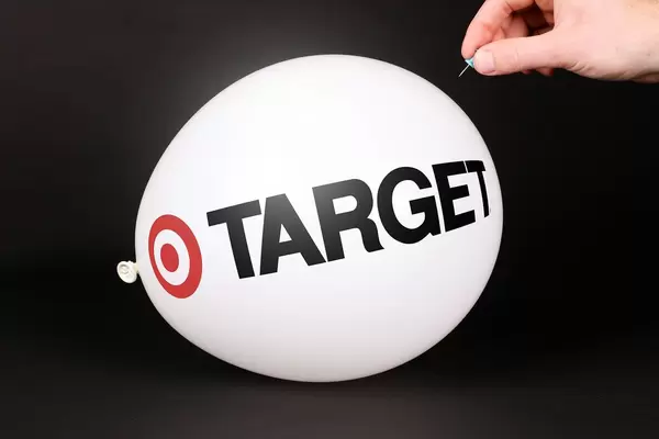 Hand uses a needle to burst a balloon with Target logo