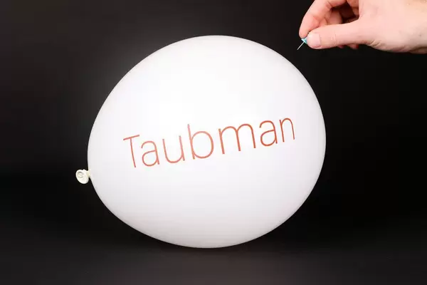 Hand uses a needle to burst a balloon with Taubman logo