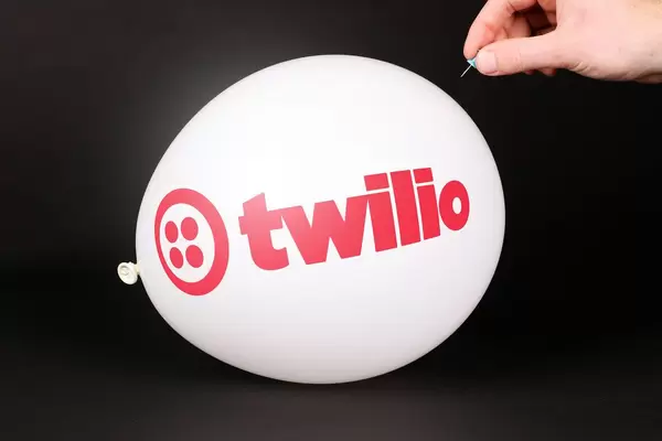 Hand uses a needle to burst a balloon with Twilio logo