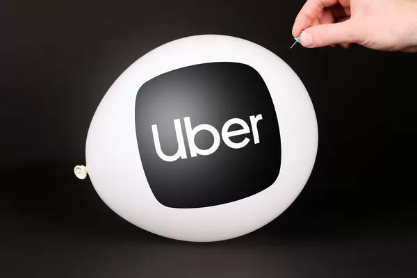 Hand uses a needle to burst a balloon with Uber logo